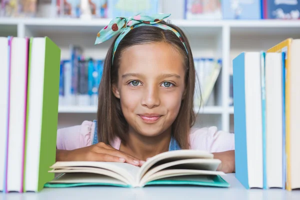 Escola menina lendo um livro na biblioteca — Fotografia de Stock