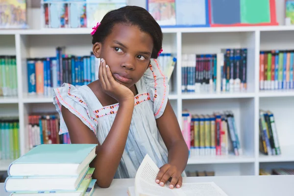 Schoolmeisje zittend op de tafel en lezing boek in bibliotheek — Stockfoto