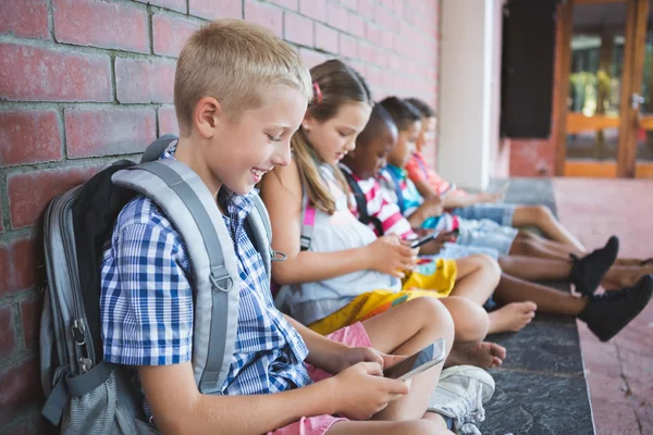 Schoolkids sedí v chodbě a pomocí mobilního telefonu — Stock fotografie