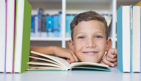 Écolier assis sur la table et lisant un livre à la bibliothèque — Photo