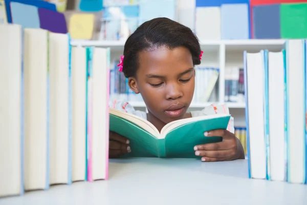 Školačka na stůl a čtení knih v knihovně — Stock fotografie