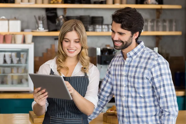 Усміхнений чоловік і офіціантка стоять за лічильником за допомогою цифрового столу — стокове фото