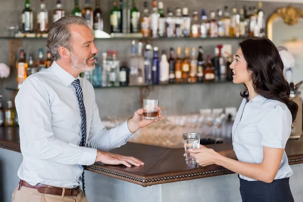Empresário e mulher de pé no balcão do bar tendo bebida — Fotografia de Stock