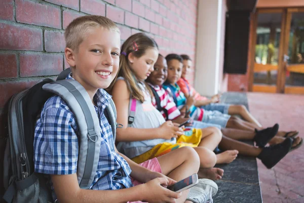 Schoolkids sitting in corridor and using mobile phone — Stock Photo, Image