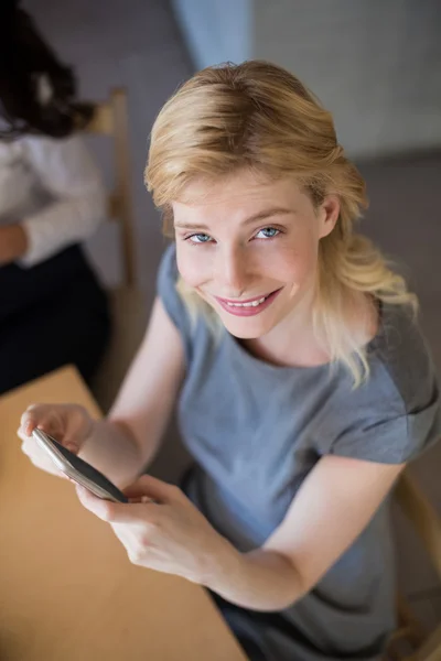 Mulher bonita sentada na mesa e usando telefone celular — Fotografia de Stock