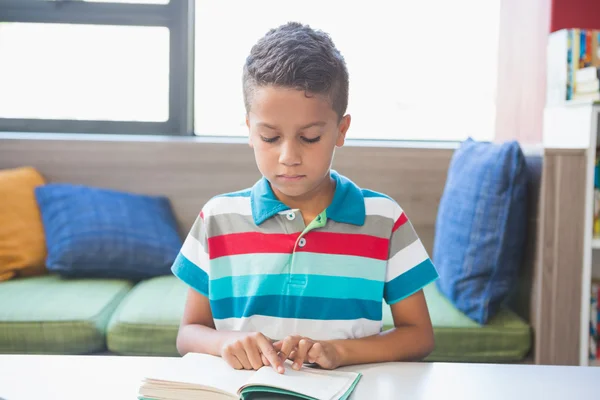 Schooljongen lezen van een boek in de bibliotheek — Stockfoto