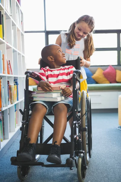 Happy schoolgirl carrying schoolboy in wheelchair — Stock Photo, Image