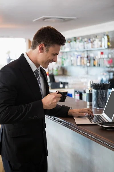 Empresário segurando uma xícara de café enquanto usa laptop — Fotografia de Stock