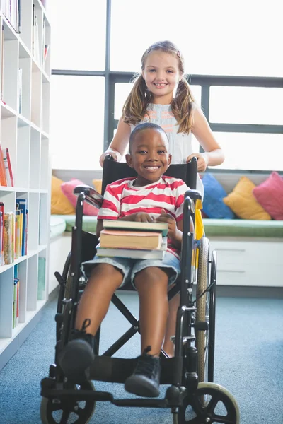 Happy schoolgirl carrying schoolboy in wheelchair — Stock Photo, Image