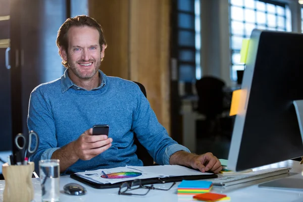 Businessman with cellphone at computer desk — Stock Photo, Image