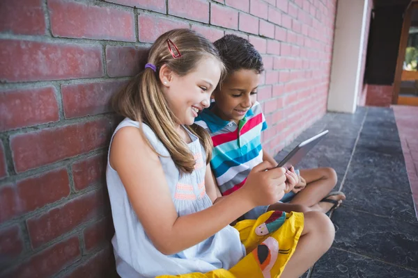 Colegiales sentados en el pasillo y usando tabletas digitales — Foto de Stock