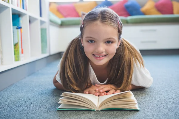 Skolflicka liggande på golvet och läsa en bok i biblioteket — Stockfoto