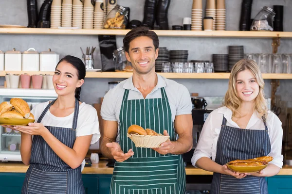 Усміхнений офіціант і дві офіціантки тримають тарілку хлібних рулонів — стокове фото