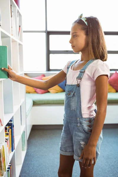 Chica tomando un libro de estantería en la biblioteca —  Fotos de Stock