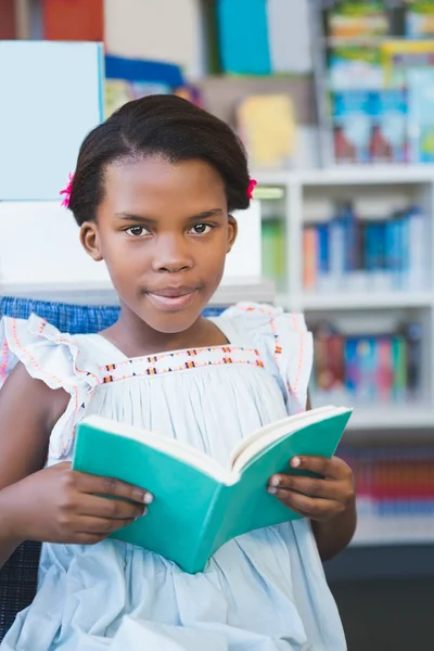 Skolflicka sitter på stol och läser bok i biblioteket — Stockfoto