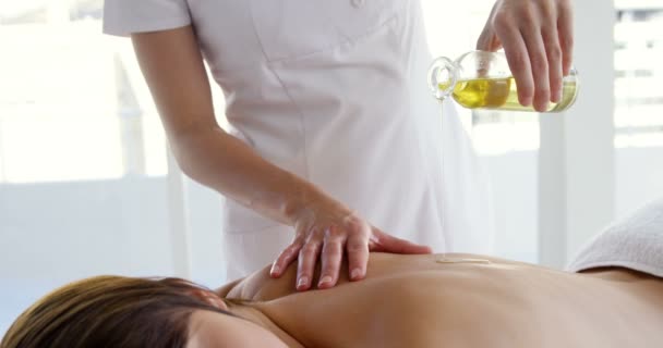 Massaggiatore versando olio sul retro del suo paziente — Video Stock
