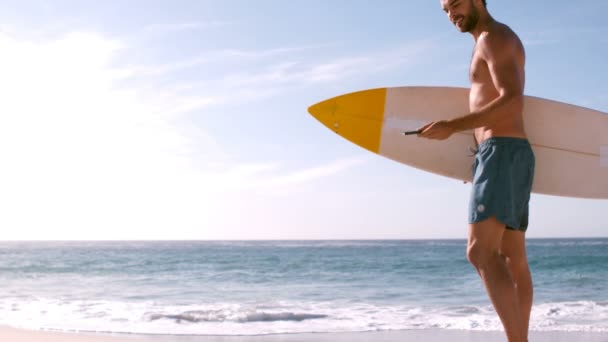 Surfista sorrindo usando seu smartphone antes de ir para a água — Vídeo de Stock