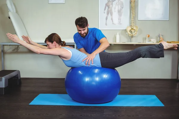 Physiotherapist assisting woman on exercise ball — Stock Photo, Image