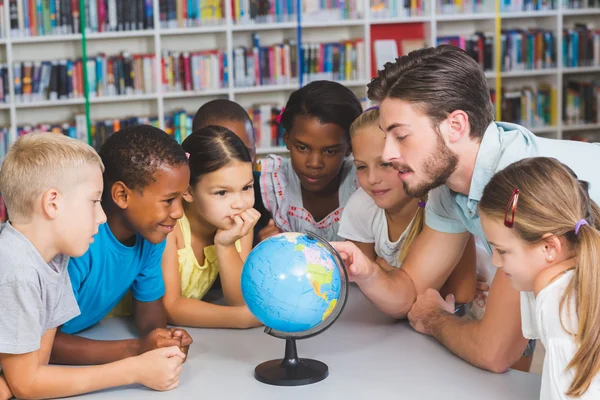 Pupils and teacher looking at globe in library — Stock Photo, Image