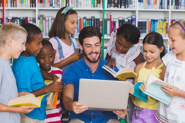 Учитель обучает детей на ноутбуке в библиотеке — стоковое фото