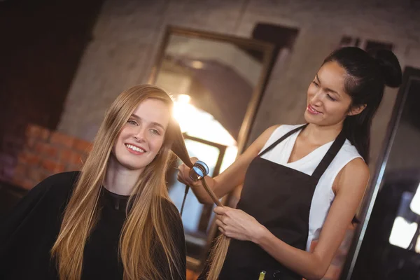 Женщина-парикмахер выпрямляет волосы клиента — стоковое фото