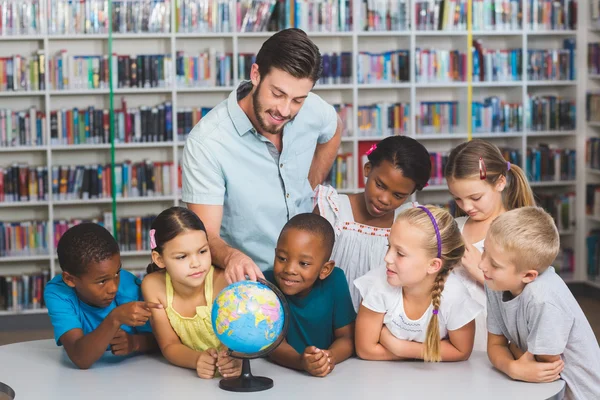 Учні та вчителька дивляться на глобус у бібліотеці — стокове фото