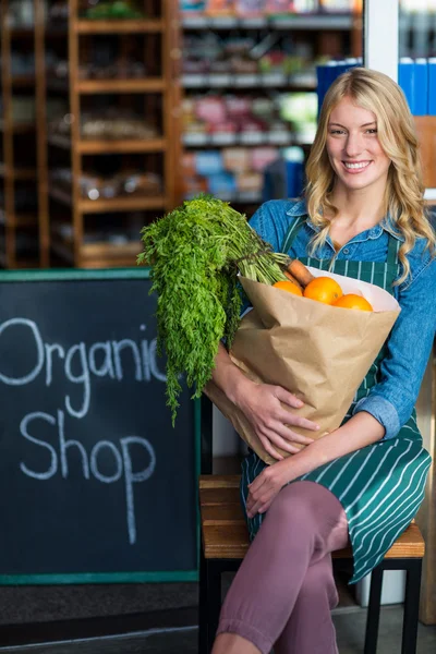 Lachende vrouw met kruidenier zak zitten in biologische winkel — Stockfoto