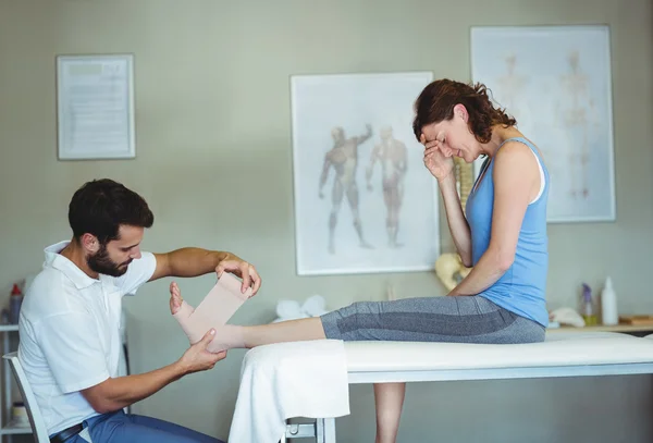 Physiotherapist putting bandage on injured feet — Stock Photo, Image