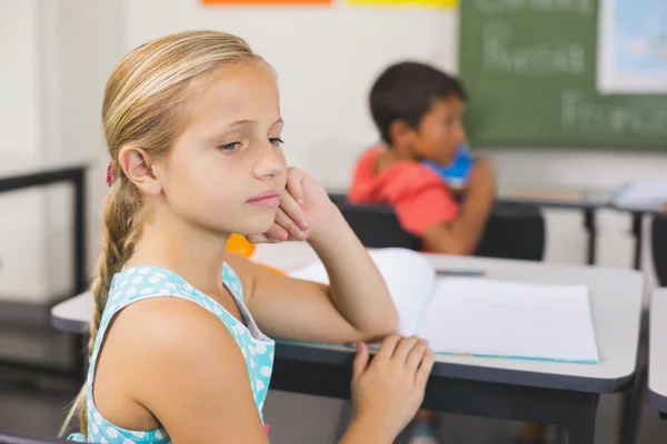 Продумана шкільна дівчина сидить за столом з рукою на обличчі — стокове фото