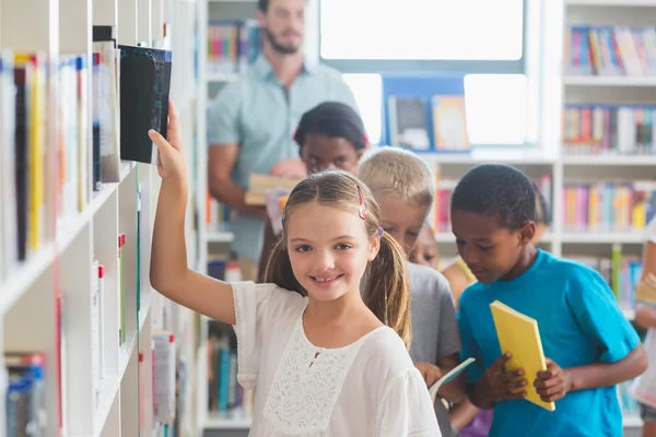 Sorrindo menina removendo livro de estante na biblioteca — Fotografia de Stock