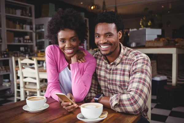 Young couple using mobile phone in cafeteria — Stock Photo, Image