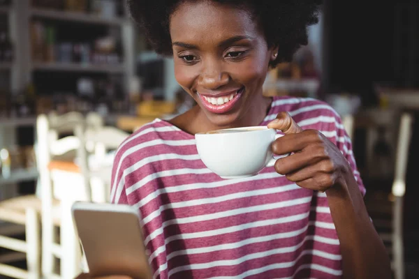 Жінка використовує мобільний телефон, маючи чашку кави — стокове фото