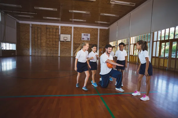 Sports teacher teaching school kids to play basketball — Stock Photo, Image