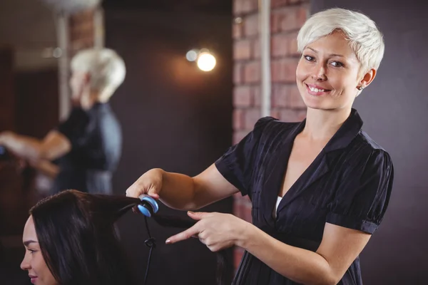 Cabeleireiro feminino alisando o cabelo de um cliente — Fotografia de Stock