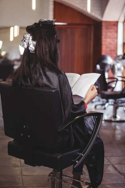 Woman reading a magazine while waiting with hair dye — Stock Photo, Image