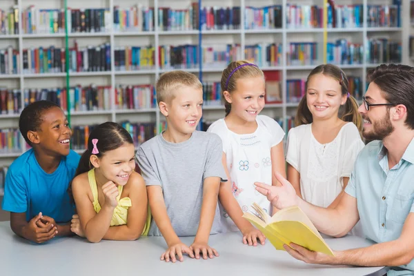 Profesor y niños leyendo libro en la biblioteca —  Fotos de Stock