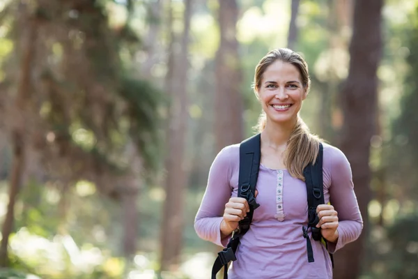 Mujer sonriente de pie en el bosque llevando mochila — Foto de Stock