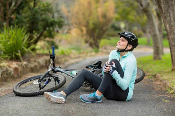 Ciclista feminina com dor segurando sua perna ferida — Fotografia de Stock