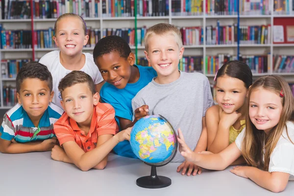 Portrait of school kids looking at globe in library — Stock Photo, Image