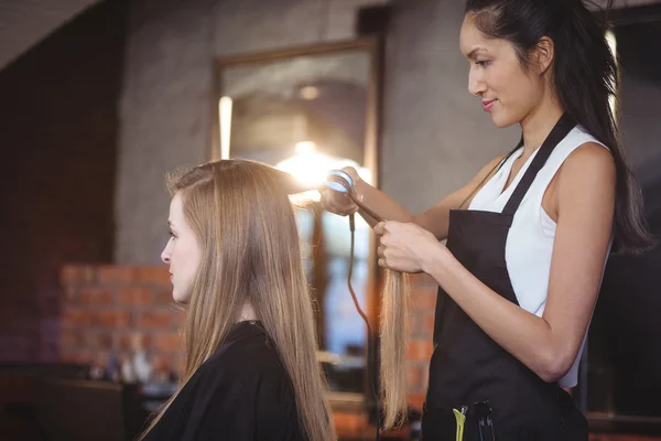 Femme coiffeuse redressant les cheveux d'un client — Photo