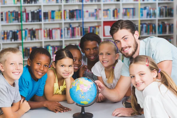 Alunos e professor olhando para o globo na biblioteca — Fotografia de Stock