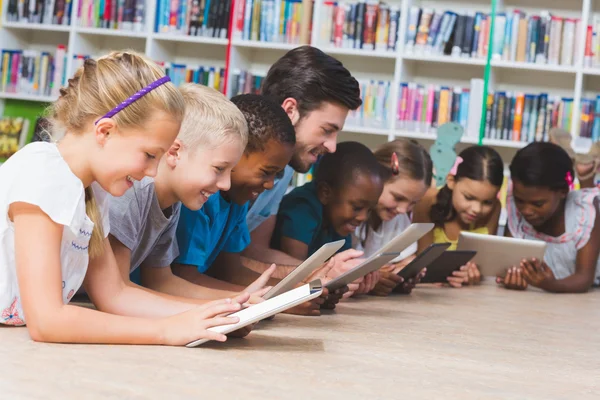 Вчитель і діти лежать на підлозі за допомогою цифрового планшета в бібліотеці — стокове фото