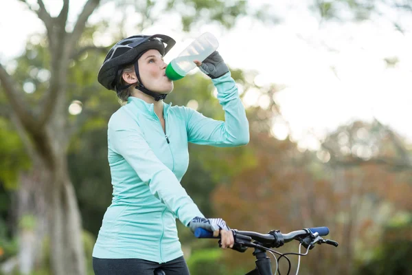 Ciclista donna acqua potabile nella foresta — Foto Stock