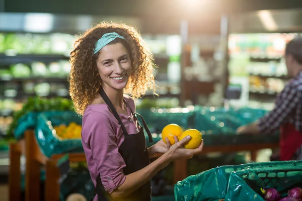 Smiling female staff holding fruits in organic section