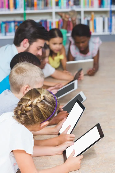 Lärare och barn liggande på golvet med digital tablet i biblioteket — Stockfoto
