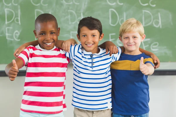 Smiling kids showing thumbs up in classroom Stock Picture