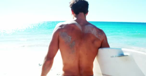Человек, стоящий на пляже с доской для серфинга — стоковое видео