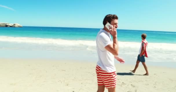 Mannen lopen op het strand tijdens het gesprek op de telefoon — Stockvideo