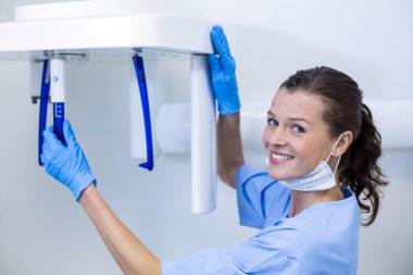 Dental assistant adjusting x-ray equipment clipart