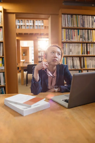 Nachdenkliche junge Frau benutzt Laptop in Bibliothek — Stockfoto